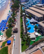 Vista aérea de praia com guarda-sóis coloridos e resort à beira-mar com piscina.