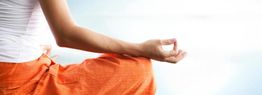 Person meditiert im Freien und trägt orange Kleidung. Links Arm in Meditationshaltung.