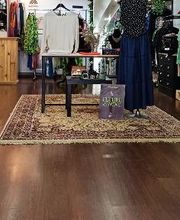 Tienda de ropa con maniquíes, alfombra y prendas exhibidas. Ambiente acogedor y colorido.