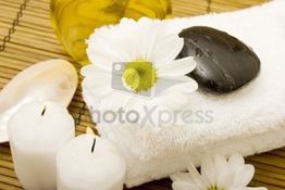 Wellness-Szene mit Handtuch, Kerzen, Blume und Stein auf Bambusmatte.