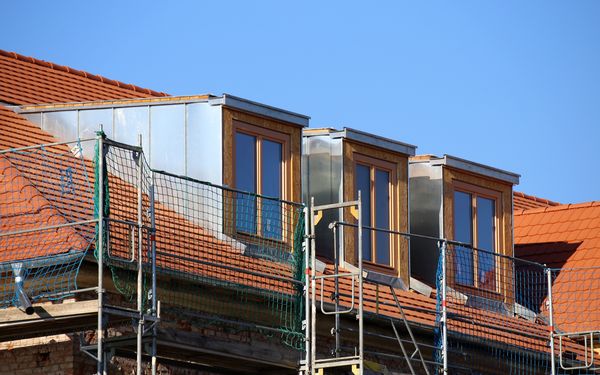 Nachträglich eingebaute Dachgauben auf einem Dach, um das Gebäude steht ein Baugerüst.