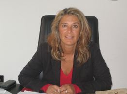 Eine Frau sitzt an einem Schreibtisch und lächelt in die Kamera.