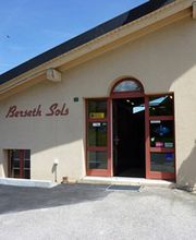 Gebäude mit der Aufschrift "Bersetth Sols", roter Tür und Blumen an der Wand, bei Sonnenschein.