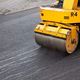 Yellow road roller compacting fresh asphalt on a street.