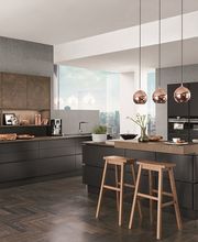 Moderna cucina con isola centrale, mobili scuri e lampade a sospensione ramate.