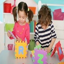 Two children playing with colorful alphabet blocks at a table in a playroom.