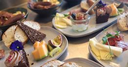 Tallerkener med morgenmad: brød, ost, kage, frugt og skål med yoghurt og bær.