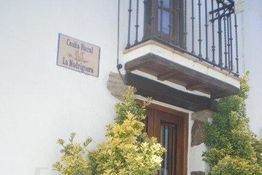 Fachada de casa rural con balcón, cartel y plantas en la entrada.