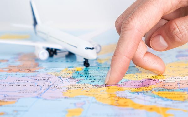 Finger zeigt auf einer Weltkarte auf ein Land neben Miniflugzeug