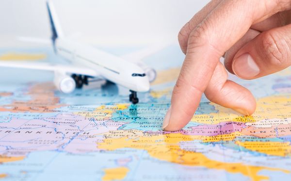 Finger zeigt auf einer Weltkarte auf ein Land neben Miniflugzeug