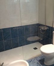 Baño moderno con ducha de vidrio, inodoro y bidé sobre baldosas azules y blancas.