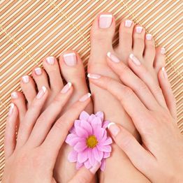 Hands and feet with French manicure, holding a pink flower on a bamboo mat background.