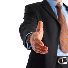 Person in a suit extending a hand for a handshake, against a white background.