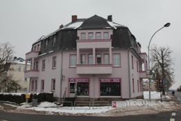Eckhaus in Rosa mit Schneedecke, Modegeschäft im Erdgeschoss. Winterliche Straßenszene.