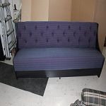 Purple and black futon in a room with beige walls and a checked item nearby.
