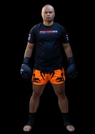 Man in boksuitrusting met zwarte handschoenen en oranje shorts poseert op zwarte achtergrond.