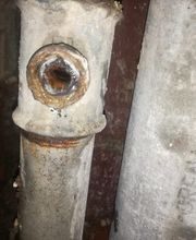 Tubería metálica oxidada con una conexión lateral, ubicada junto a otra tubería similar.