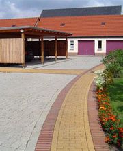 Gepflasterter Hof mit Blumenbeet, Garage und überdachtem Carport an einem Wohnhaus.