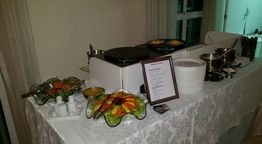 Mesa de buffet com saladas, pratos, talheres e dois crepes sendo preparados em uma chapa.