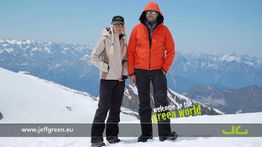 Zwei Personen in Winterkleidung auf einem schneebedeckten Berg, Alpen im Hintergrund.