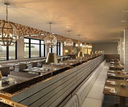 Restaurante moderno con mesas alineadas, luces colgantes y ventanas grandes a la izquierda.