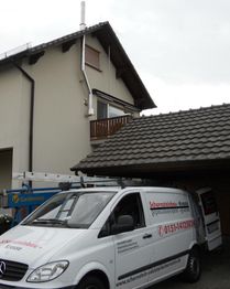 Transporter vor Haus mit Schornsteinbau-Aufschrift, daneben Carport und Leiter, bewölkter Himmel.