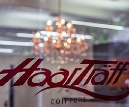 Friseursalon-Schriftzug „HaarTräff“ auf Fenster, im Hintergrund ein Kronleuchter.