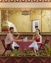 Pareja cenando pizza en una terraza decorada con plantas y luces suaves.