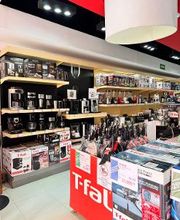 Tienda de electrodomésticos con cafeteras y ollas en estantes y cajas de marca T-fal en el frente.
