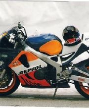 Rennmotorrad mit Repsol-Design, blau-orange-weiß. Aufsitzender Helm über dem hinteren Sitz.