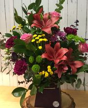Ramo de flores coloridas en florero sobre mesa de madera, con fondo de pared blanca desgastada.
