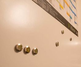 Weiße Magnettafel mit Magneten und einem farbigen Kalender oben rechts.