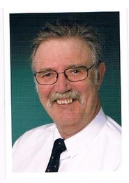 Älterer Mann mit Brille, Schnurrbart und Krawatte lächelt in die Kamera.