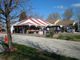 Outdoor yard sale under a red and white tent with people browsing items on a sunny day.