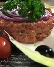 Rindertatar mit Petersilie, Zwiebeln, Tomaten und Oliven, auf einem Salatblatt serviert.
