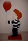 Holzfigur eines Jungen mit roten Haaren und gestreiftem Pullover, hält einen roten Luftballon.