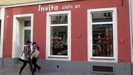 Zwei Personen vor einem roten Laden mit Schrift "Invito zieht an". Eröffnung am 25.10.
