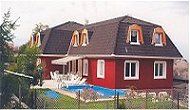 Rotes Haus mit Mansarddach, blauen Pool im Vordergrund, umgeben von Garten und Zaun.