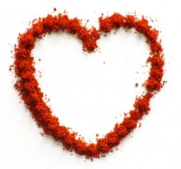 Herz aus rotem Gewürzpulver auf weißem Hintergrund.