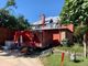 Workers repair a red house roof with a ladder; red trailer and tools nearby.