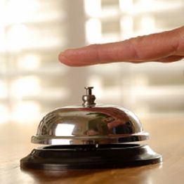 Finger pressing a shiny service bell on a wooden counter with blurred background.