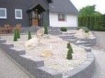 Vorgarten mit Kieselsteinen und kleinen Koniferen, umgeben von Steinmauern, neben einem Haus.