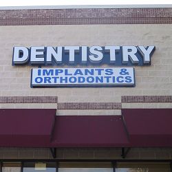Dentistry sign with "Implants & Orthodontics" on a brick building facade above a maroon awning.