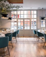 Restaurante elegante con mesas redondas, sillas verdes y grandes ventanales. Ambiente acogedor.