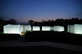 Zelte leuchten in der Dämmerung, umgeben von Bäumen und einem klaren Himmel.