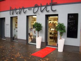 Geschäftsfassade mit Pflanzen und rotem Teppich, Schild mit "Inn-out" und Tafelangebot.