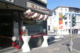 Gebäude mit Ballons und weißen Stehtischen, Ecke einer belebten Straßenkreuzung.