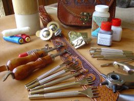 Ledertool-Sortiment mit Werkzeugen, Farben und Materialen auf einer Oberfläche arrangiert.