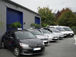 Taxis garés devant un bâtiment gris avec portails bleus, entourés de végétation.