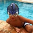 Niño con gorra de natación y gafas, sentado al borde de una piscina.